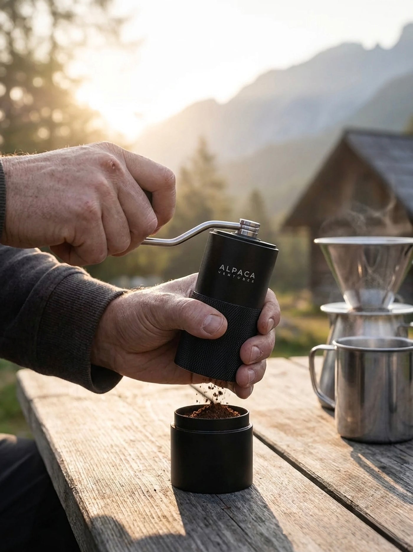 Hands using the ALPACA manual coffee grinder outdoors on a wooden surface