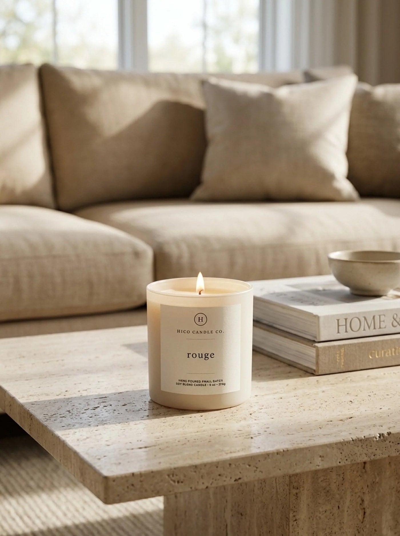 Hico Rouge candle on a linen sofa beside a stack of books.