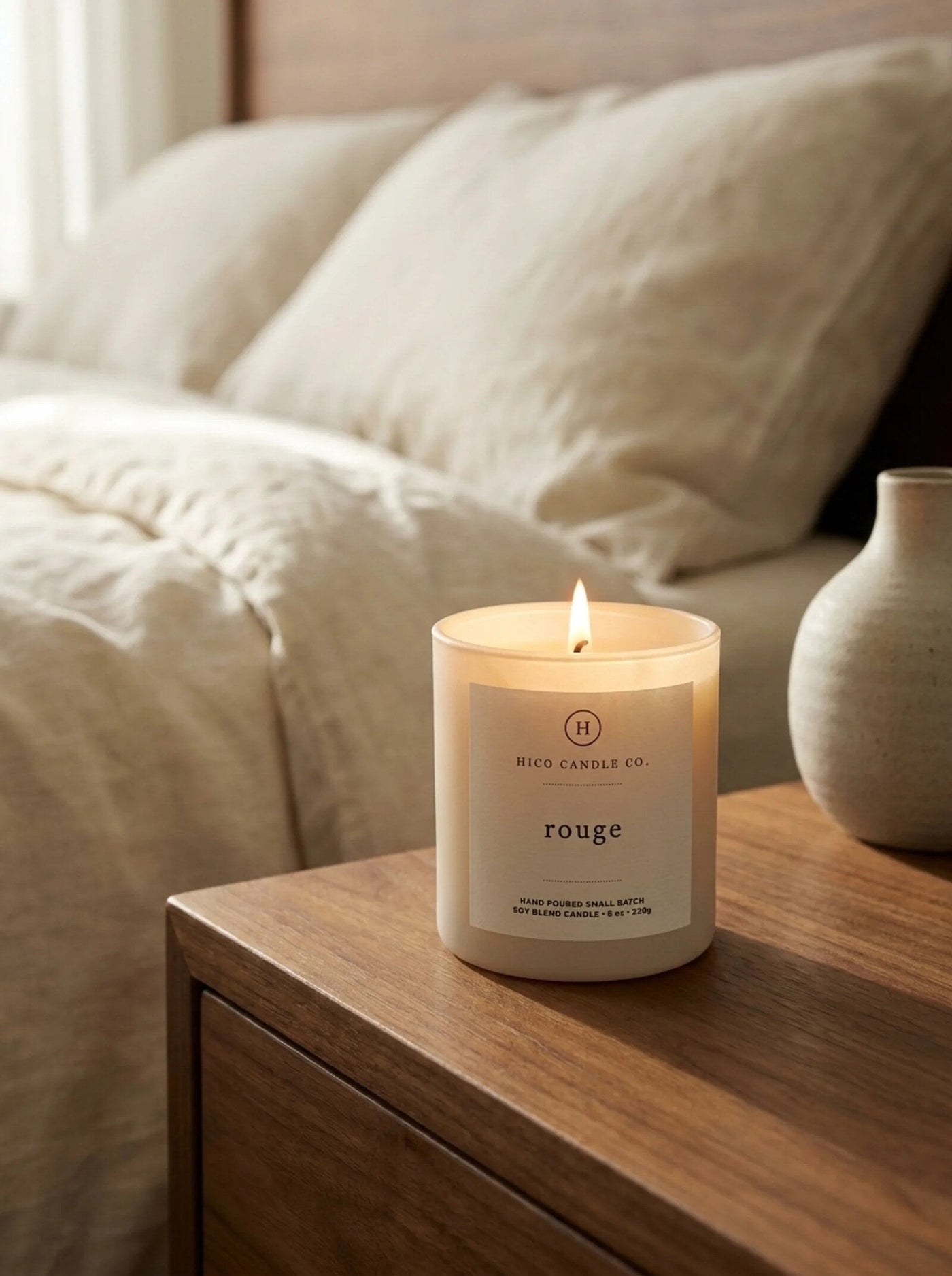 Hico Rouge candle on a bedside table with linen bedding.