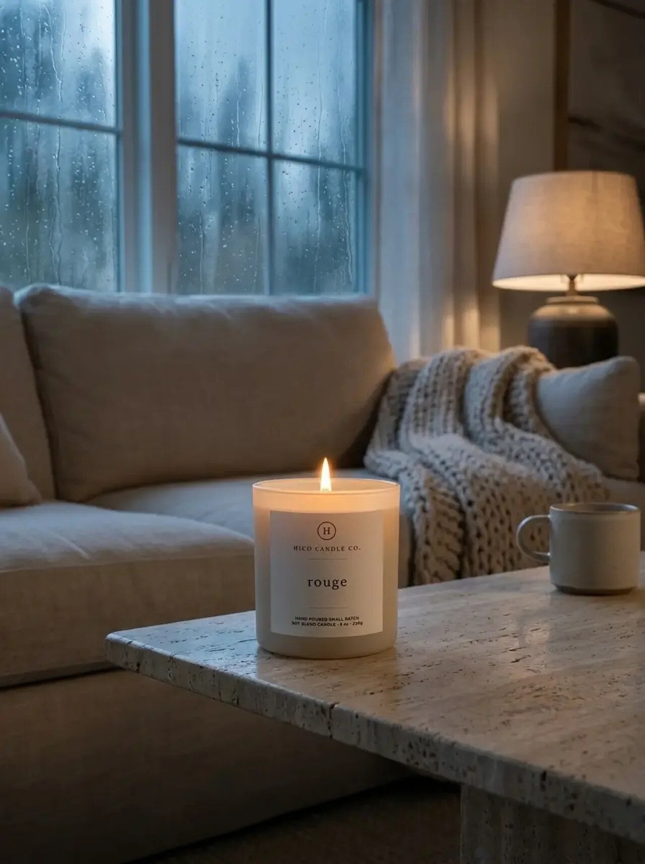 Hico Rouge candle by a window with a lamp and a knit blanket.